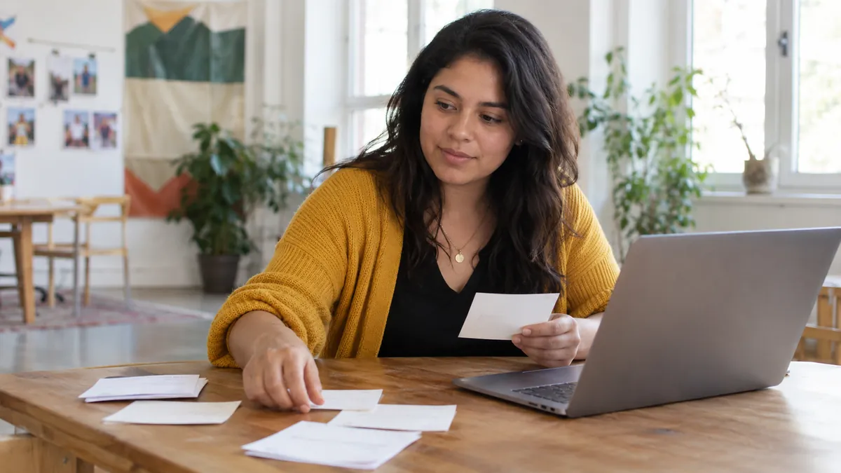 Young adult communications coordinator sorting blank notes beside one laptop in a community workshop room