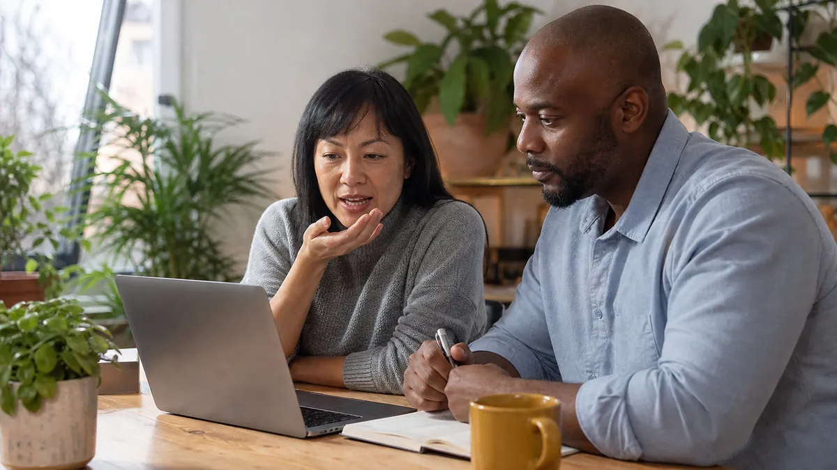 Two coworkers reviewing voice typing notes at a laptop in a plant-filled home office